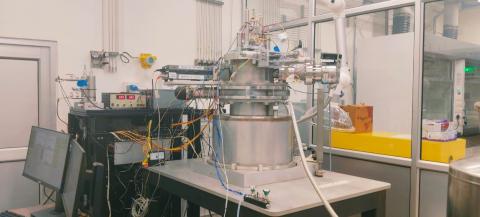 A Transient Analysis of Products (TAP) reactor setup featuring a stainless-steel ultra-high vacuum chamber mounted on a workbench, integrated with gas pulse injection systems and connected to quadrupole mass spectrometer (QMS).