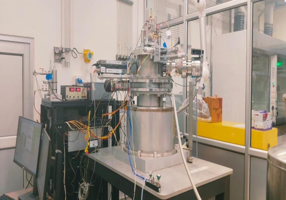 A Transient Analysis of Products (TAP) reactor setup featuring a stainless-steel ultra-high vacuum chamber mounted on a workbench, integrated with gas pulse injection systems and connected to quadrupole mass spectrometer (QMS).